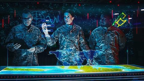 Three military officers in camouflage uniforms analyze a digital world map on a futuristic control table.