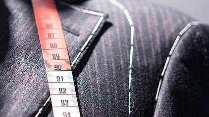 Tailored Suit with Measuring Tape Close-up of a tailored pinstripe suit with white stitching lines, draped with a red and white measuring tape showing measurements around 90 centimeters.